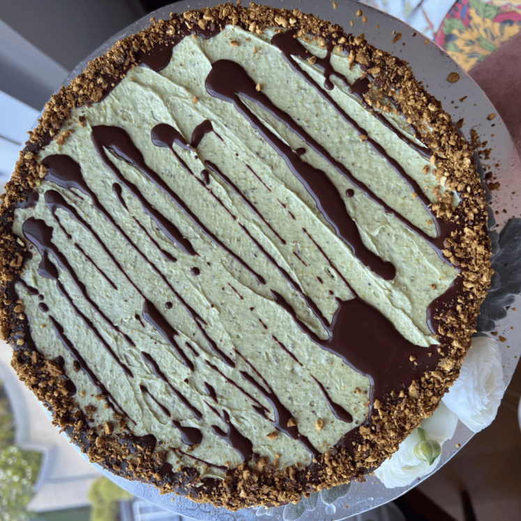 round cake with green buttercream and chocolate drizzle being held by a window
