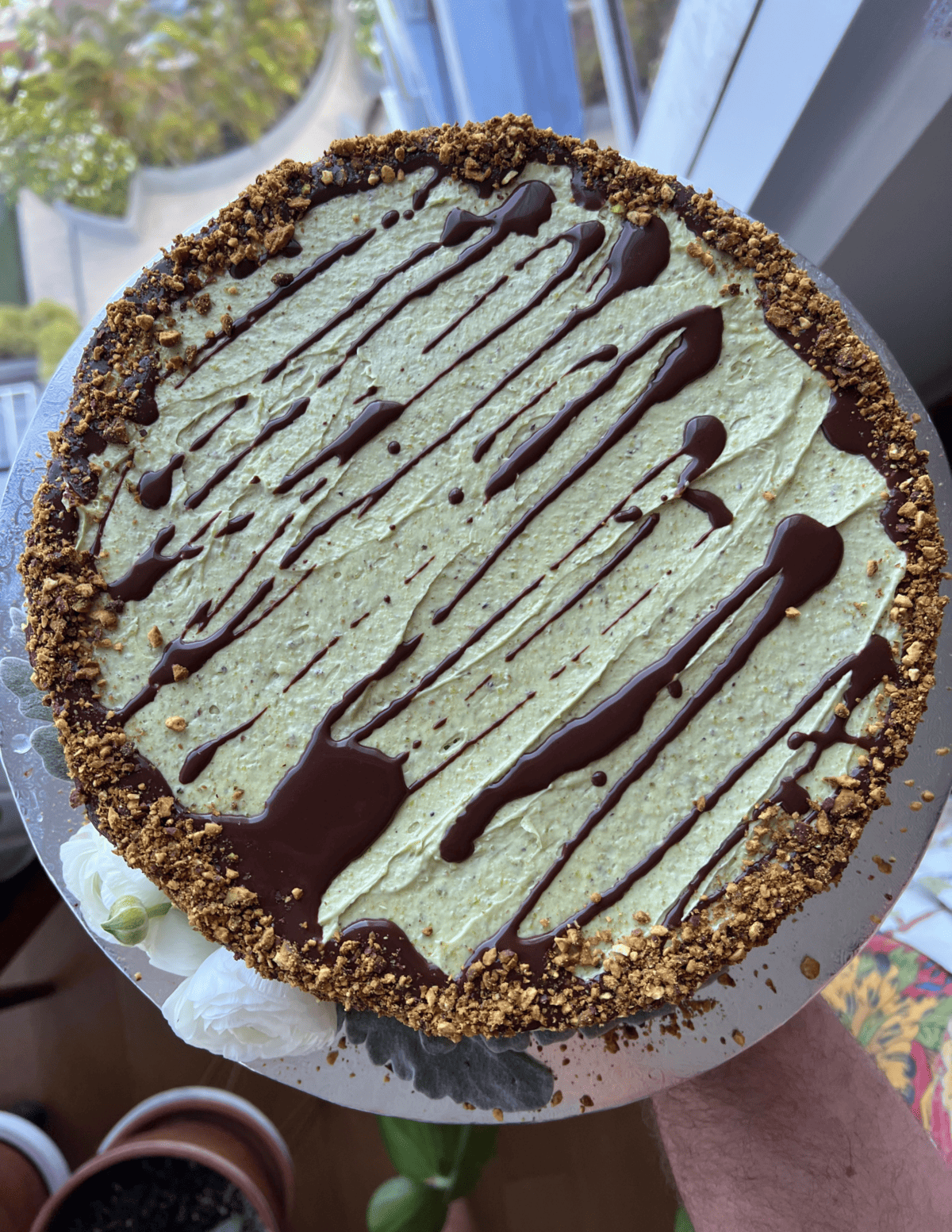 round cake with green buttercream and chocolate drizzle being held by a window