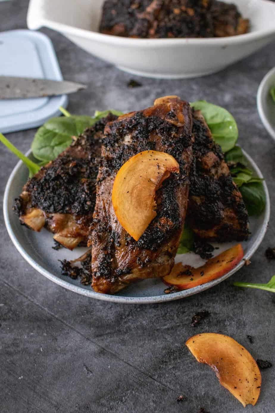 coffee rubbed ribs layered on dish served over spinach, garnished with slice of peach 