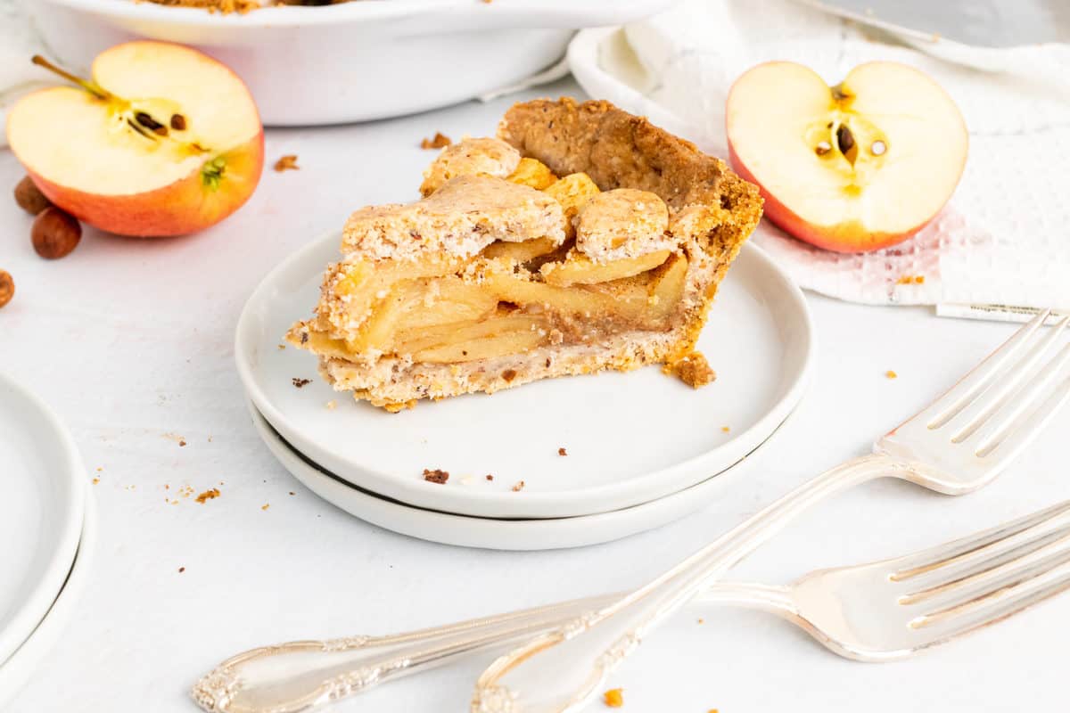 a served slice paleo apple pie on white plates with apples on the background 