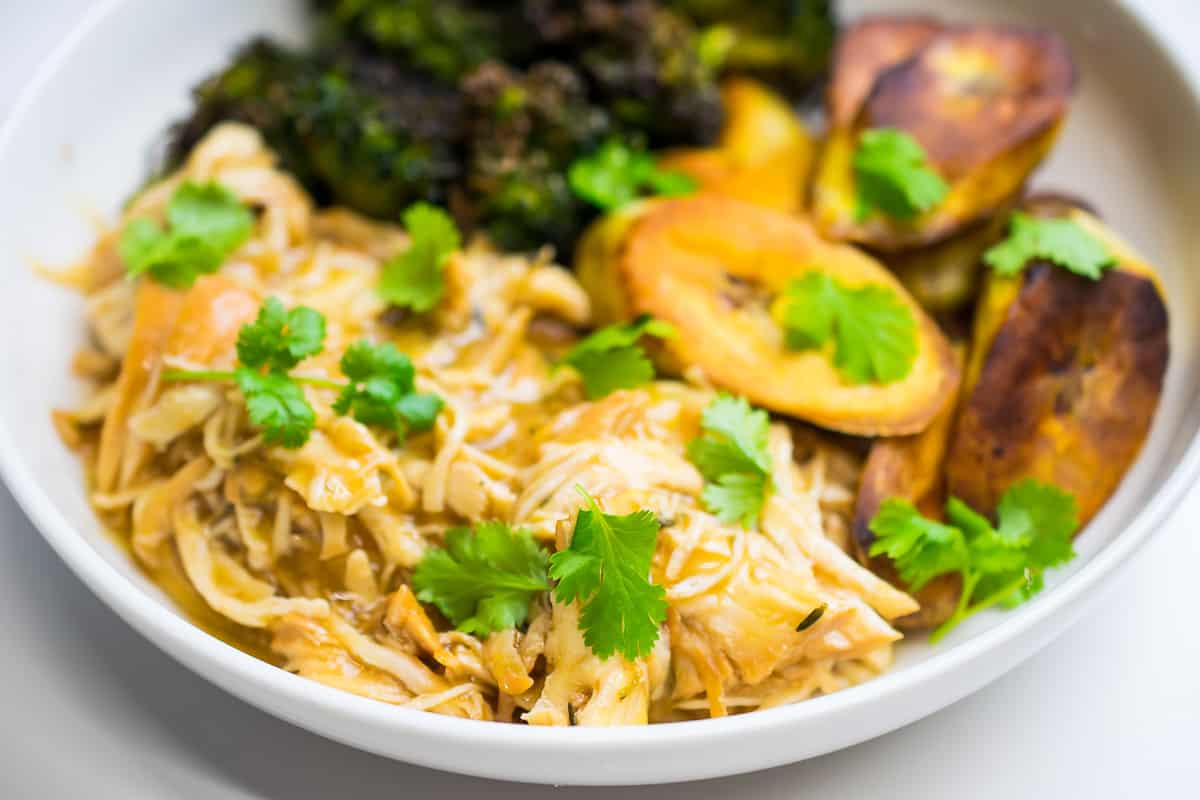 instant pot orange chicken with roasted broccoli and plantains, garnished with cilantro in a white plate