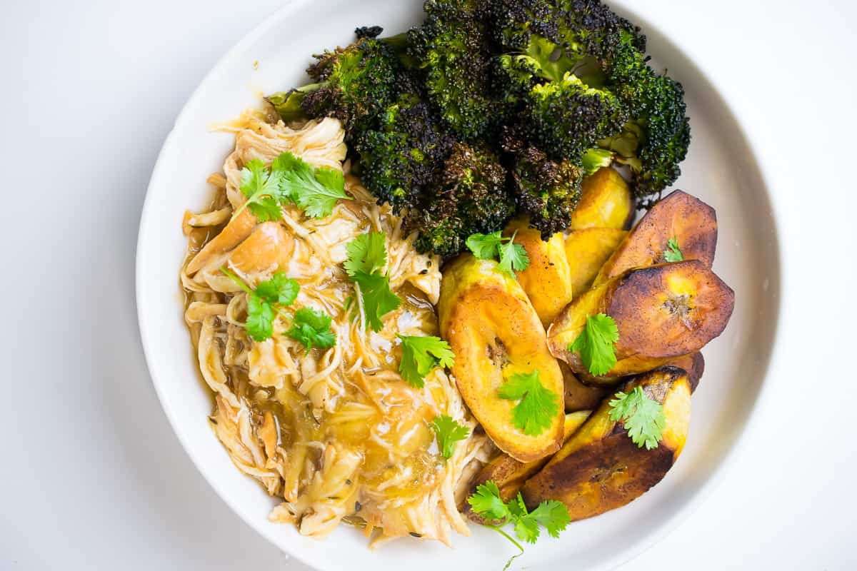 aip orange chicken in a white bowl with broccoli and plantains, garnished with cilantro