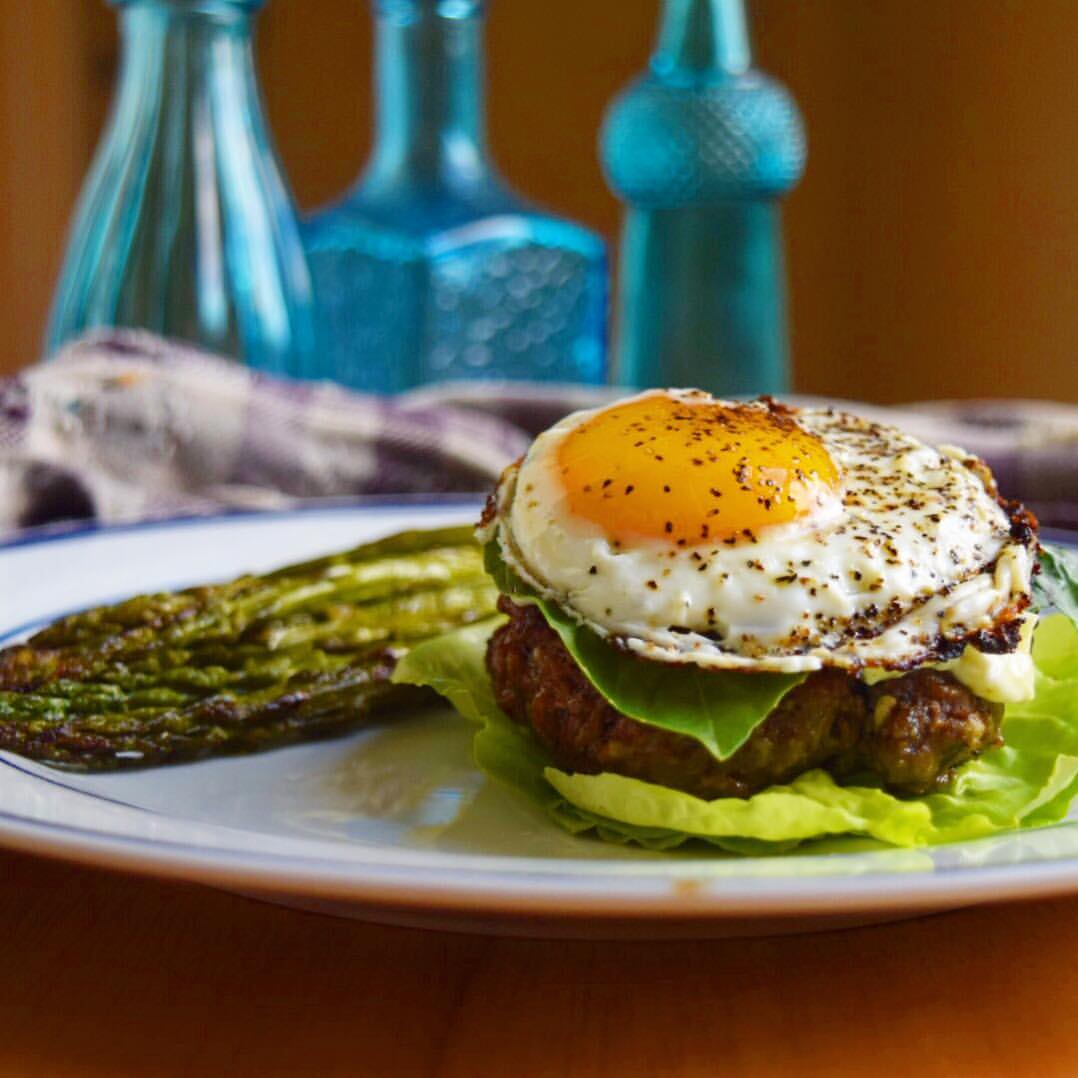 fried egg on a burger with asparagus and blue bottles in the background