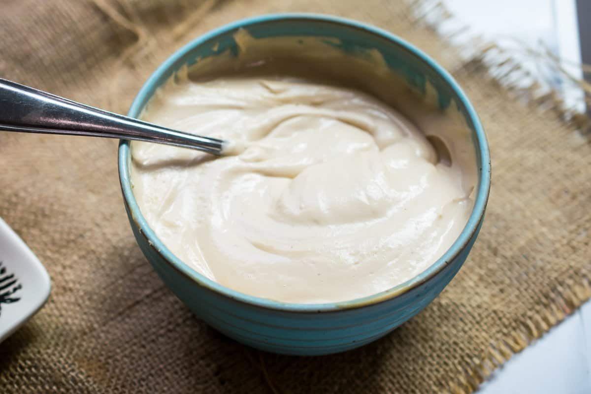 bowl of creamy dairy free cream cheese frosting with a spoon in it over burlap