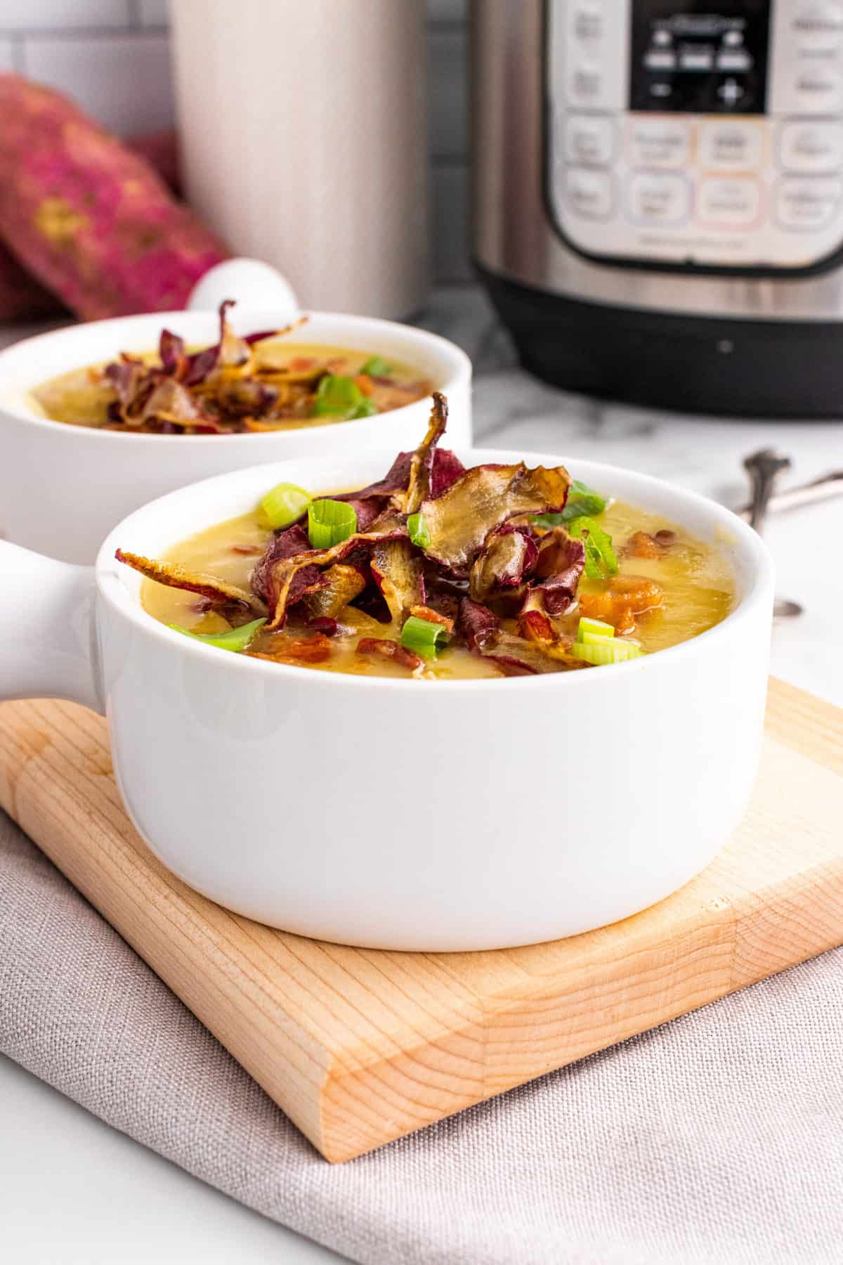 close up of a bowl of whole30 sweet potato turkey chili topped with crispy potato skins and green onion with a pressure cooker in the background