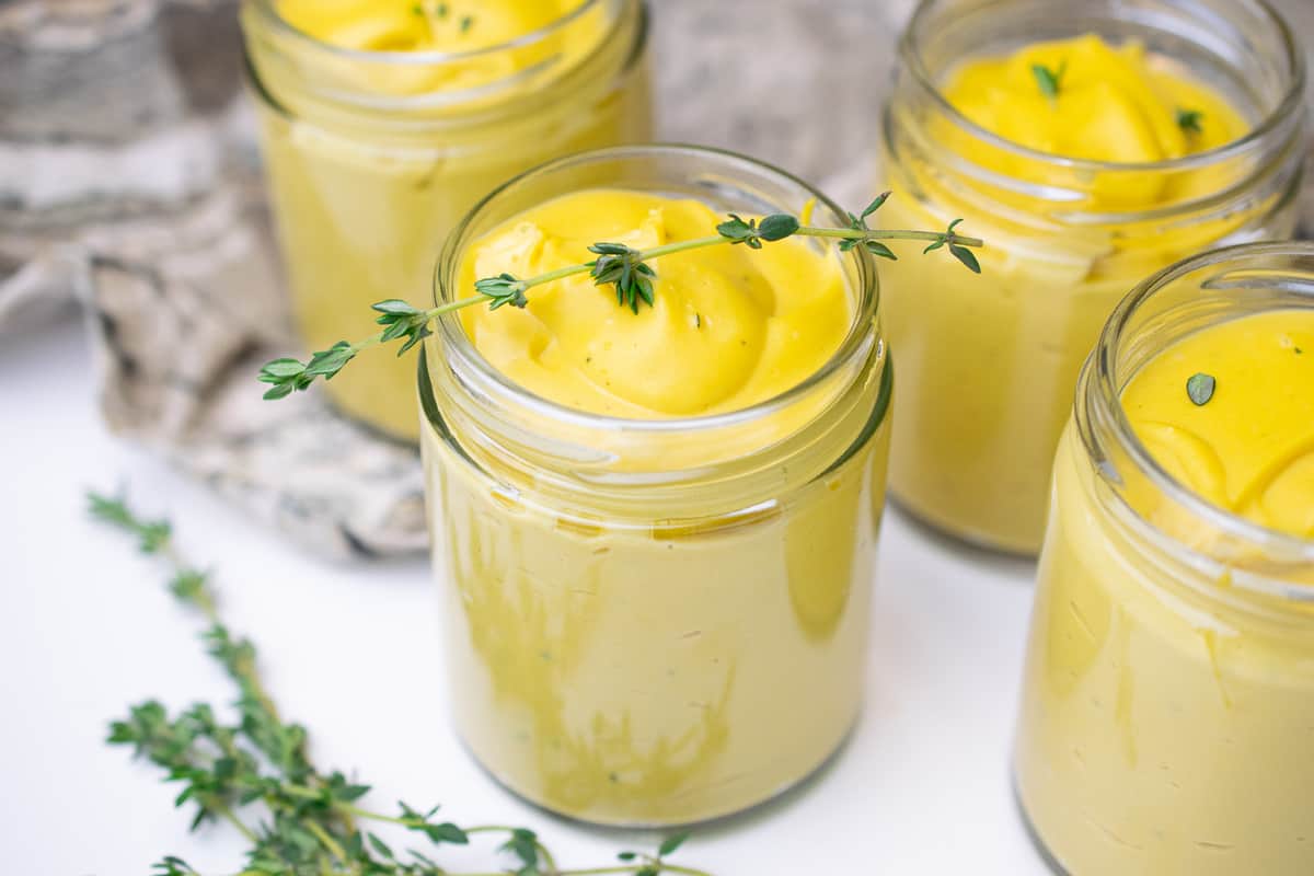 jars of vegan custard on a white counter with sprigs of thyme