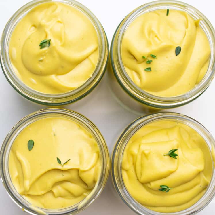 four jars of creamy vegan custard with thyme leaves on a white counter