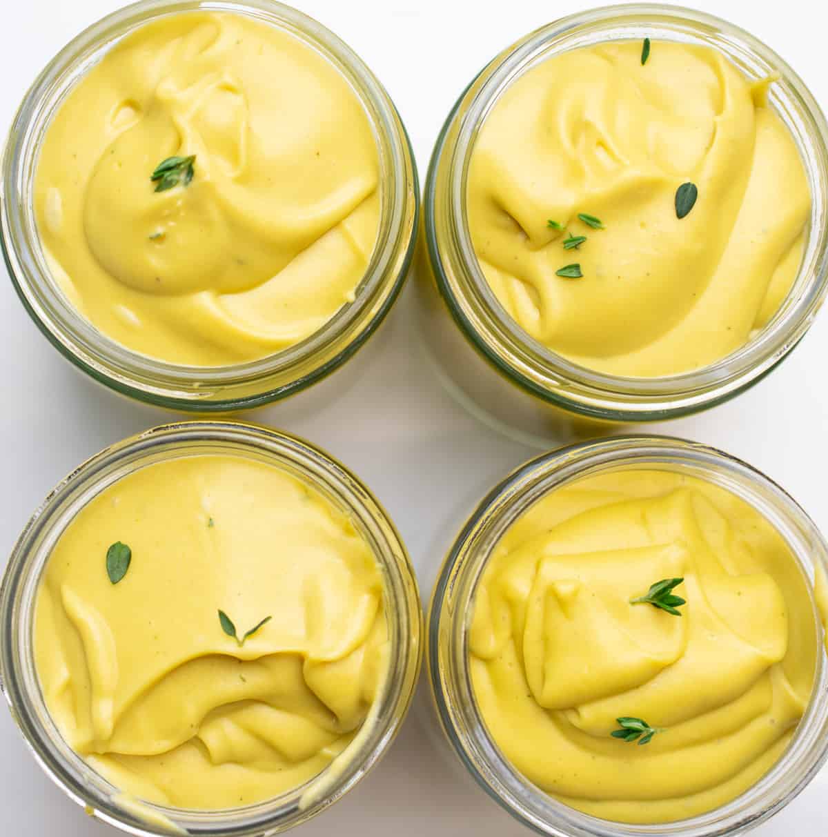 four jars of creamy vegan custard with thyme leaves on a white counter