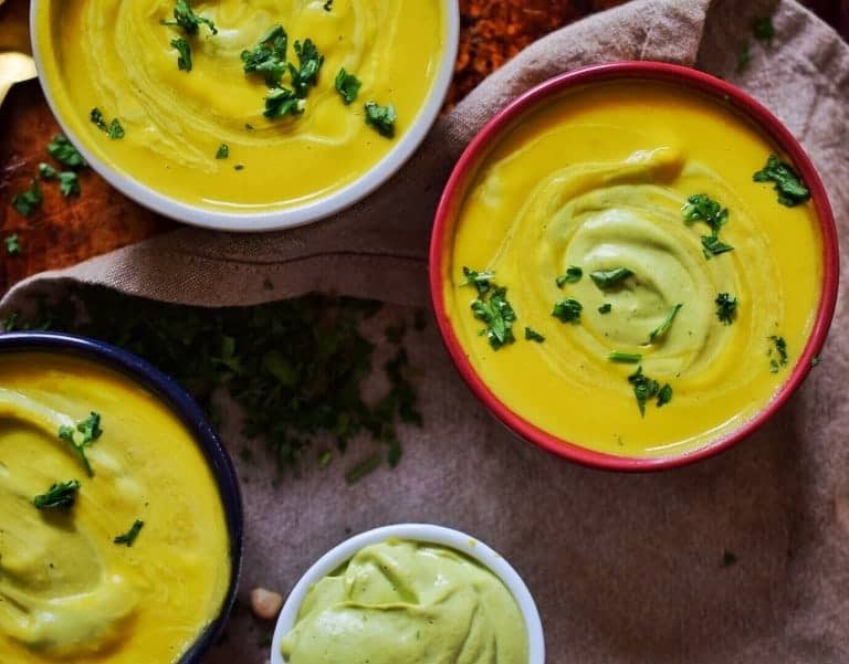 roasted butternut squash soup in small bowls with avocado cream swirl and herbs 