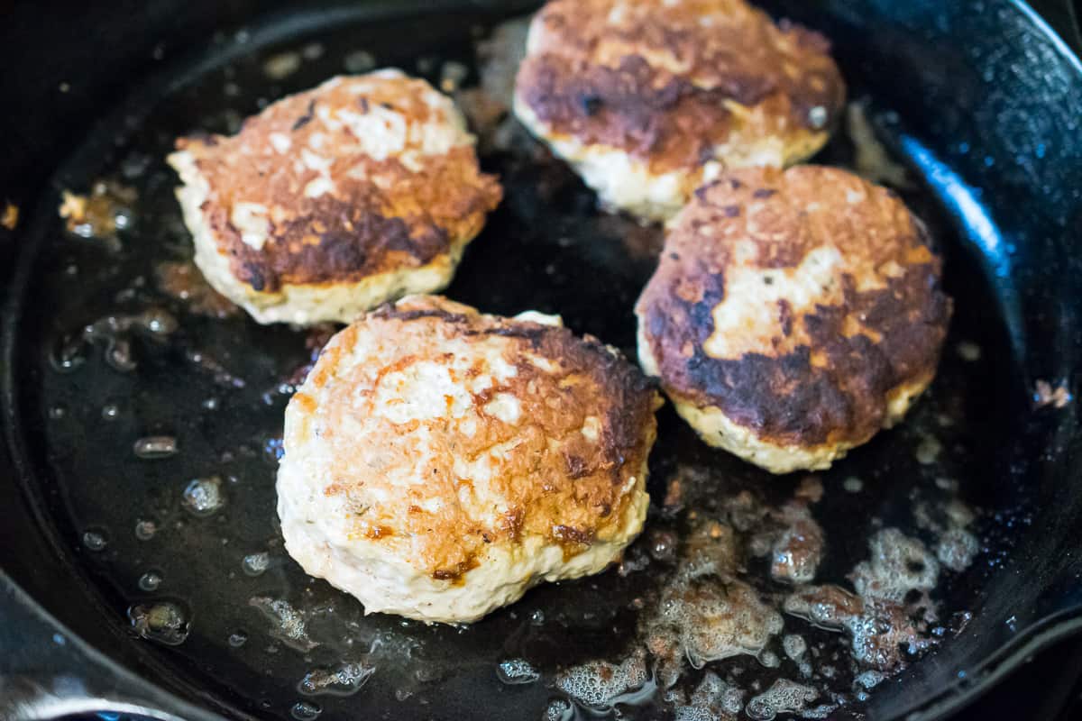 4 paleo turkey burgers being cooked up in a castiron skillet