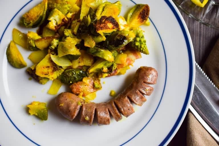 a white plate with blue rim served with a roasted bratwust and brussel sprouts