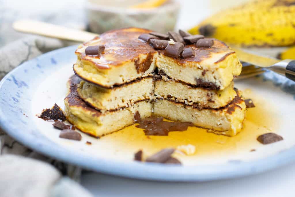 three nut free paleo banana pancakes stacked on a plate with chocolate chips and maple syrup