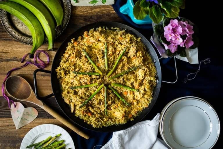 plantains, flowers, wooden spoon, and skillet with rice and vegetables on table