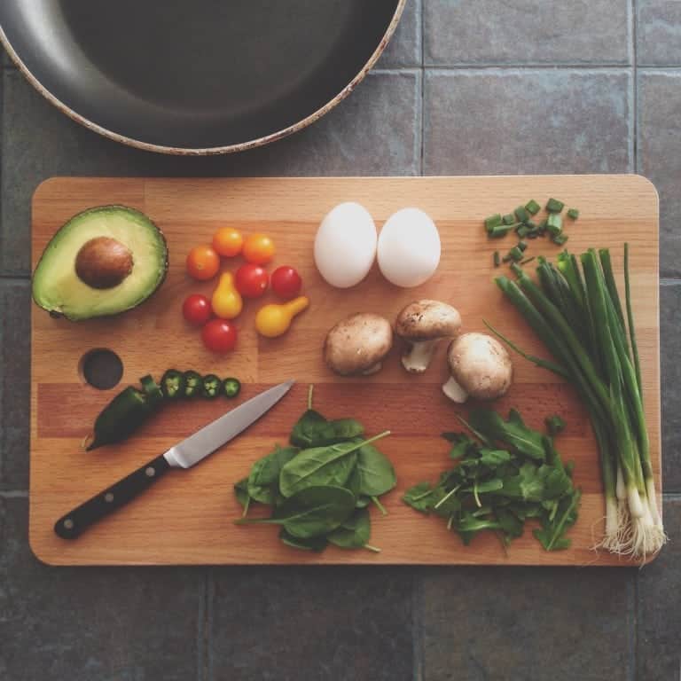 cutting board with avocado, tomato, eggs, spinach, mushrooms, and green onions