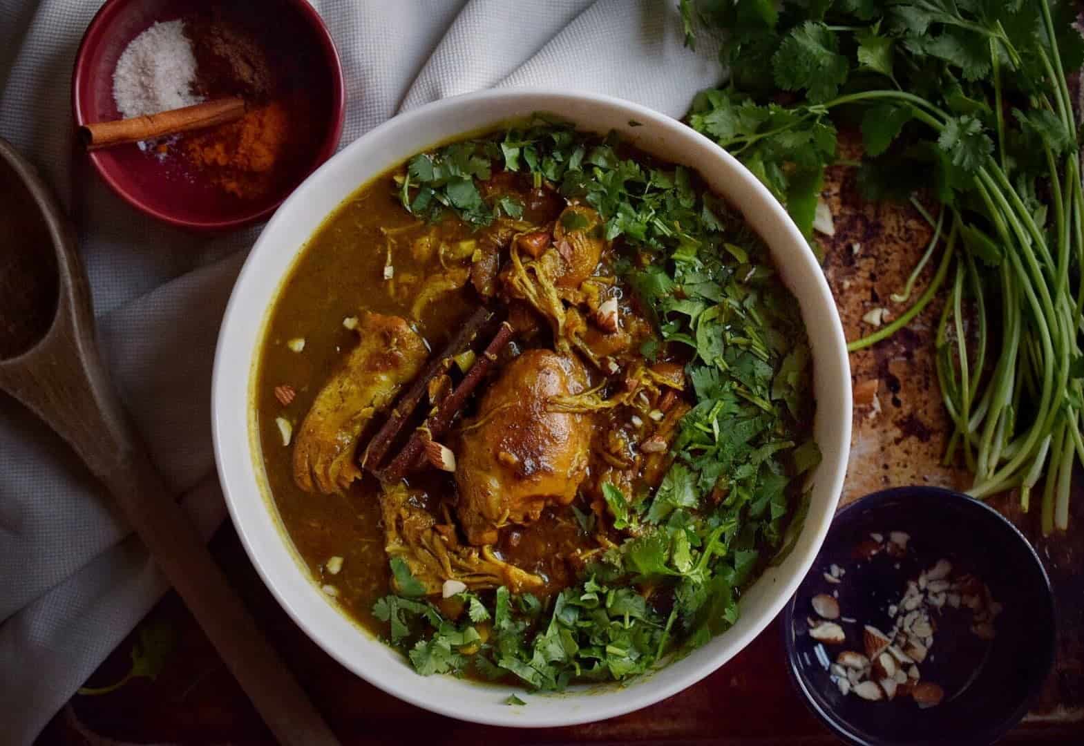 indian butter chicken in a white bowl surrounded by spices and cilantro