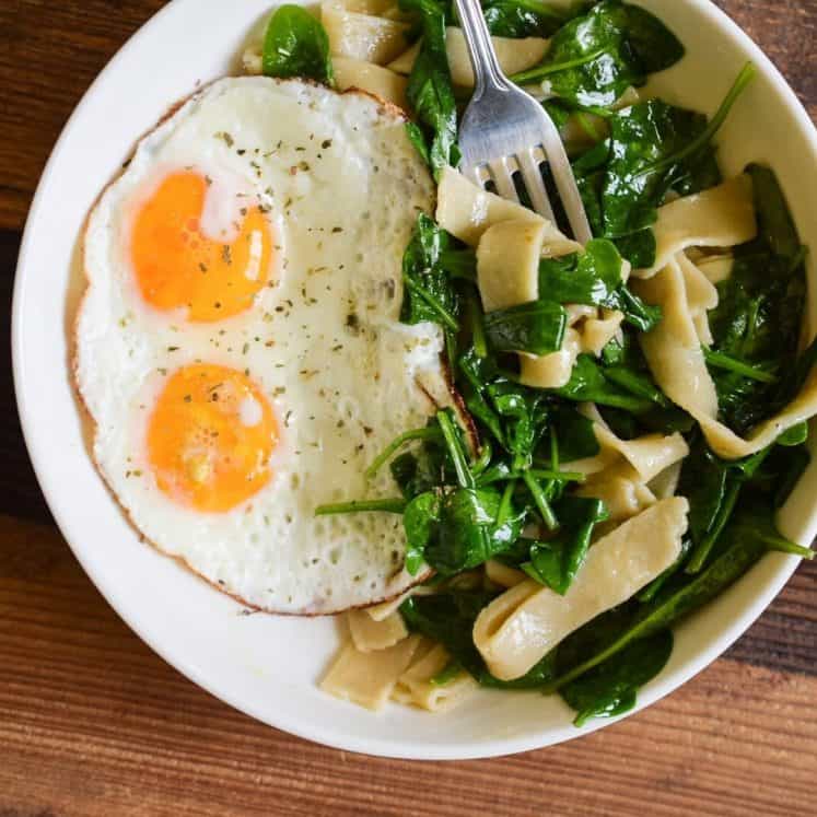 white plate with sunny side up eggs and greens and cassava flour pasta