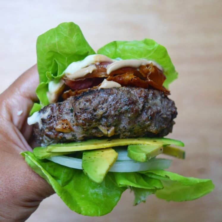 hand holding a lettuce-wrapped burger with avocado and onion