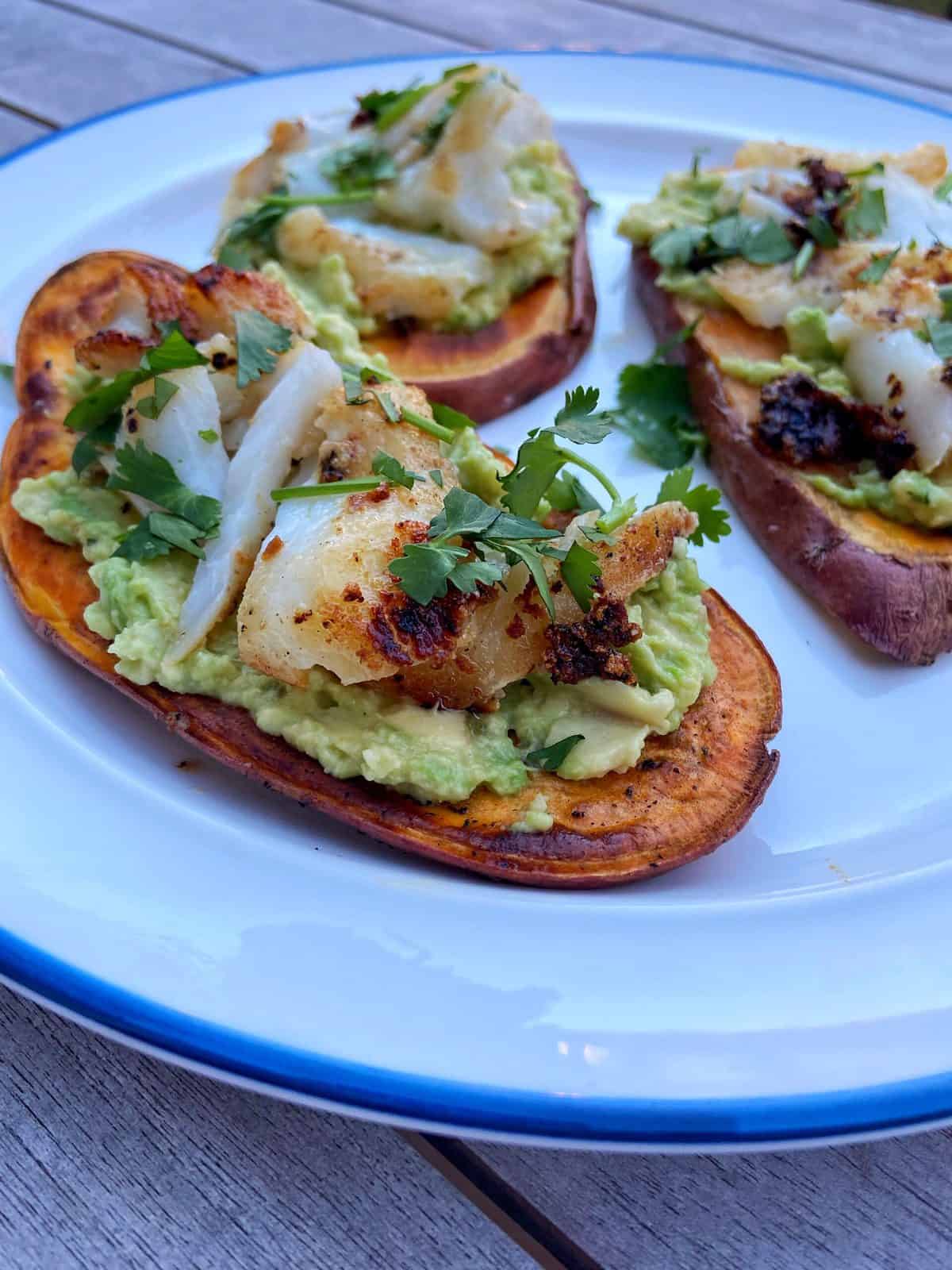 aip sweet potato toast on a white plate, loaded with avocado, fish and cilantro 