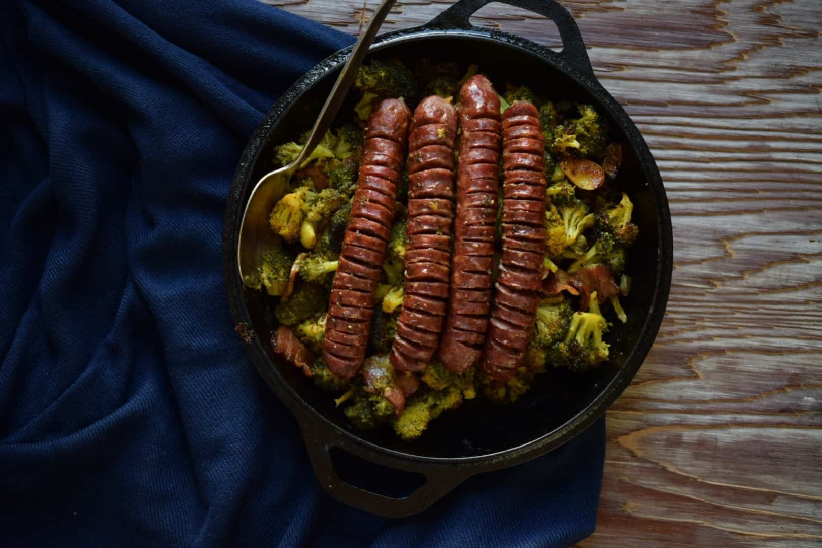 bratwust that are sliced on a bed of roasted veggies over a wood board