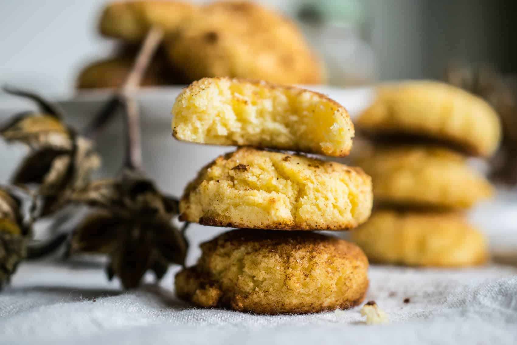 three keto snickerdoodle cookies stacked on each other with more cookies in the background 