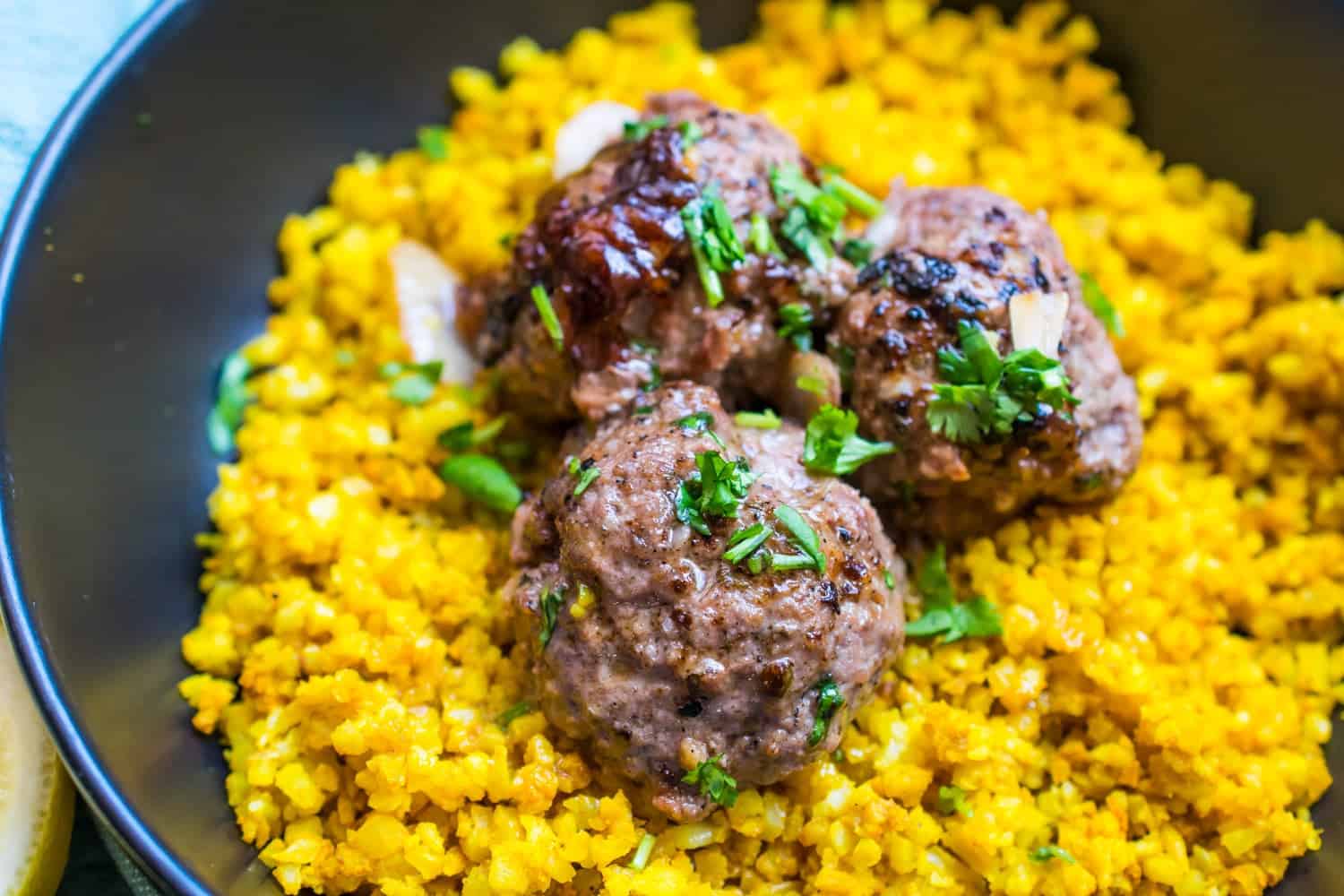 three carne asada meatballs over yellow rice in a black bowl. garnished with cilantro