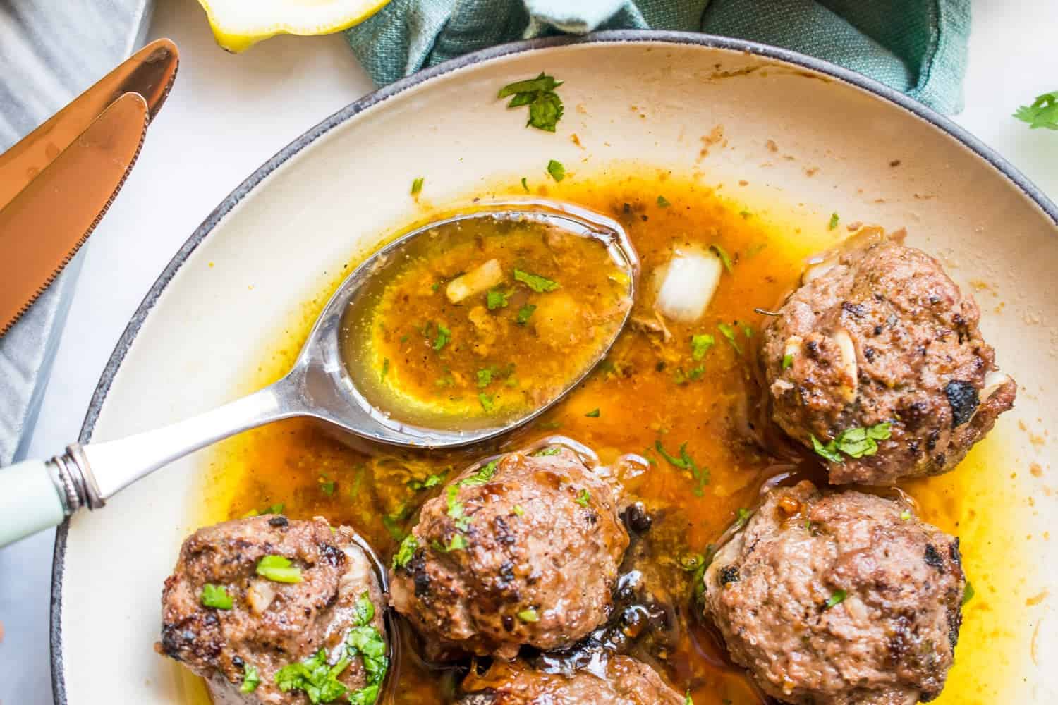 five carne asada meatballs on a plate sitting in their marinade juice with onion and cilantro on a blue-lined plate