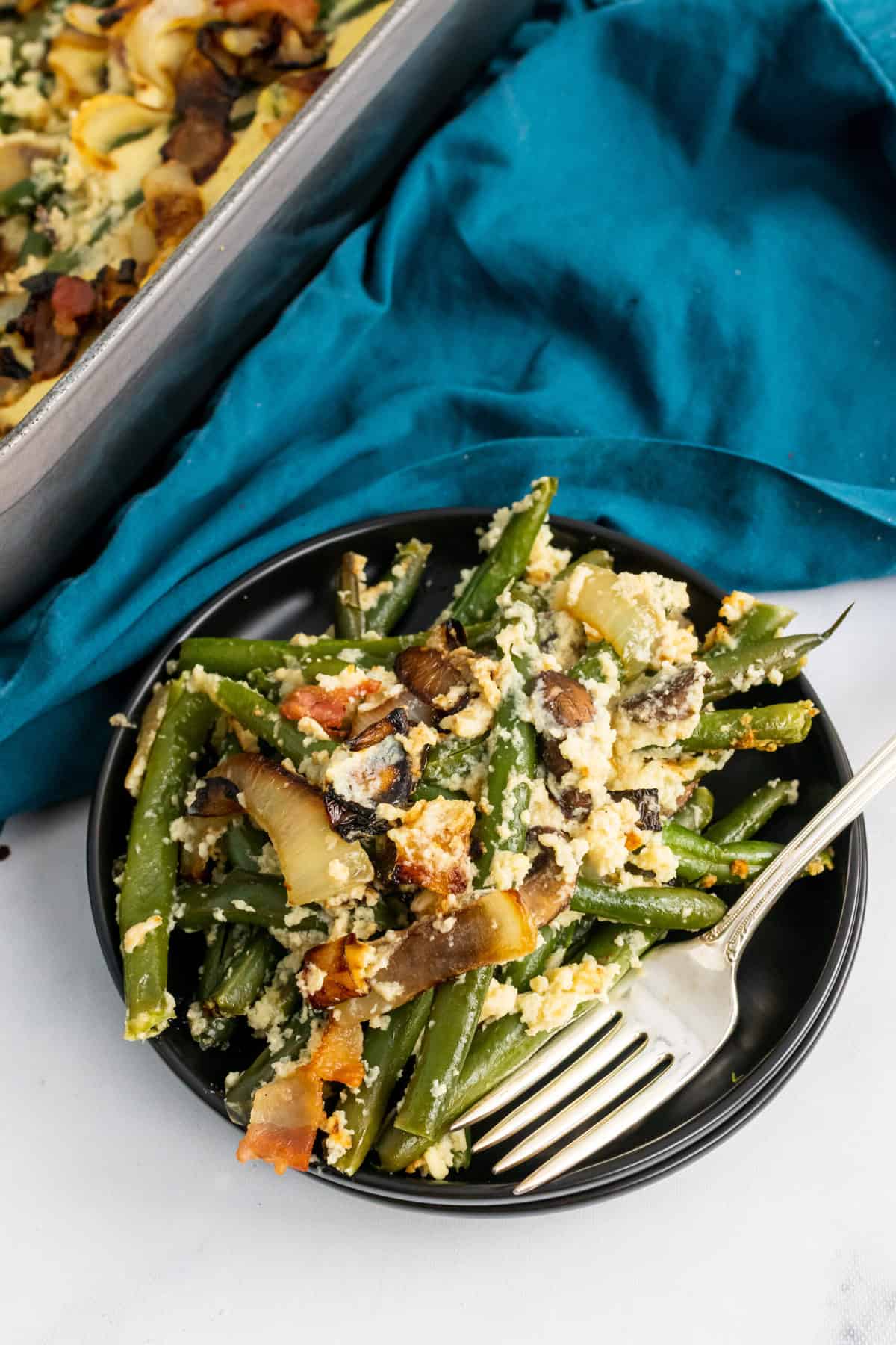 a black plate with paleo green bean casserole, a fork and blue napkin