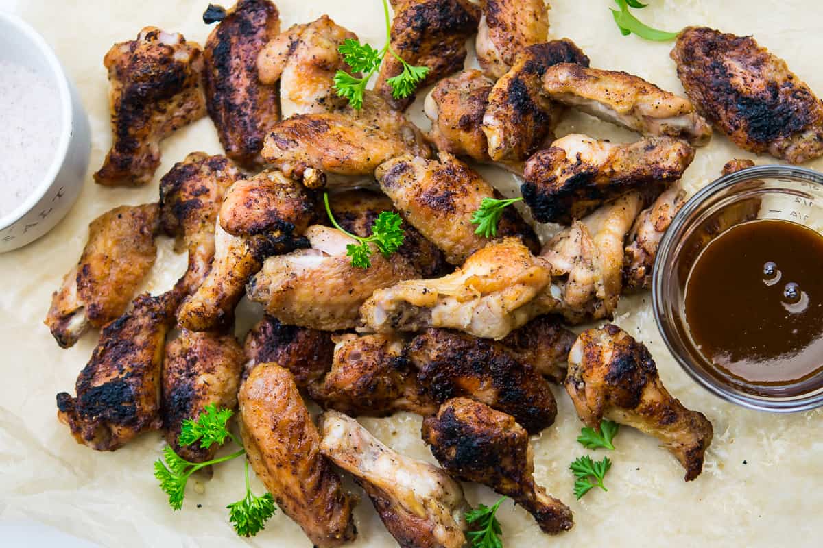 A pile of crispy Salt and Vinegar Wings on a piece of parchment paper, garnished with fresh parsley and a side of tangy vinegar sauce.