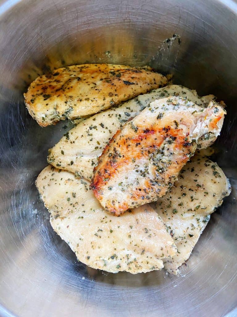 Freshly cooked, slightly caramelized seasoned chicken breasts sit in a large metal bowl.