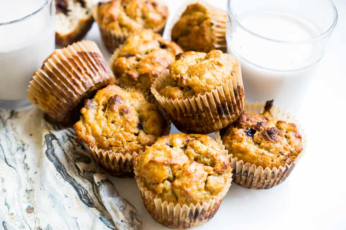 gluten free banana muffins on a white counter with a napkin and cups of milk