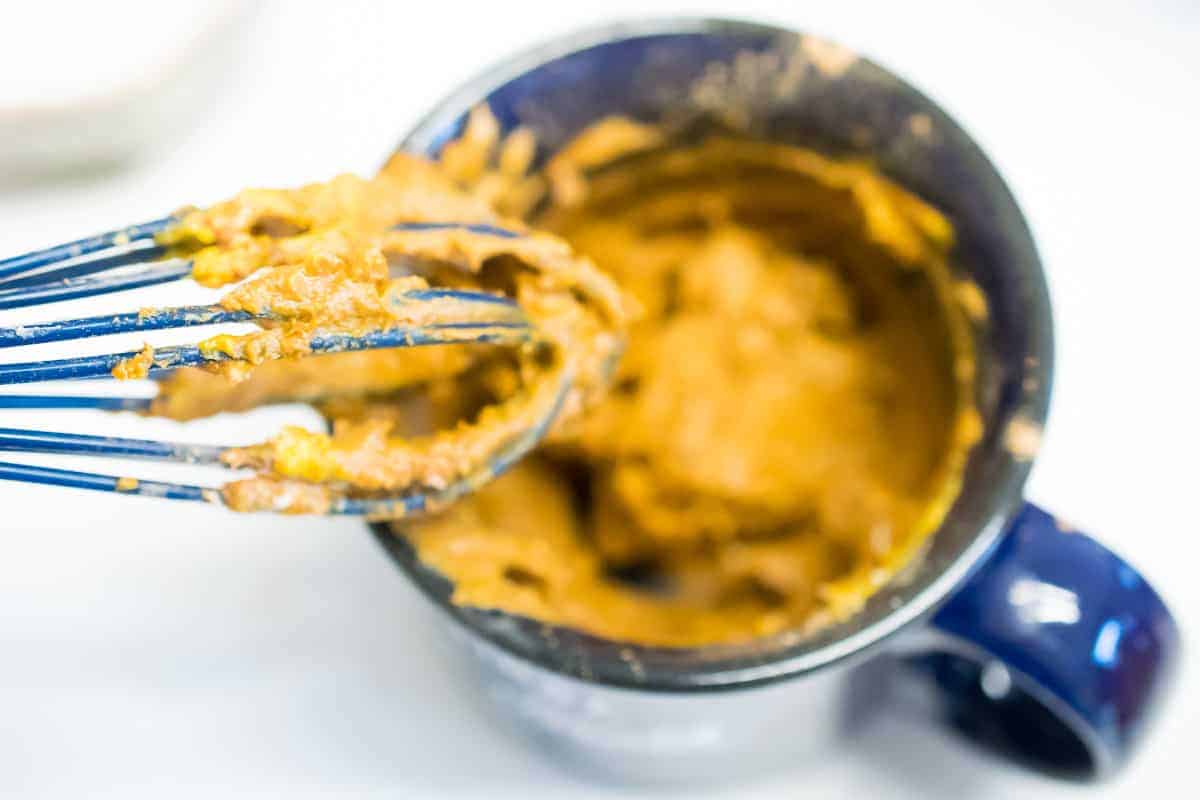 Thick AIP Brownie Mug Cake batter in a blue mug with batter stuck to a whisk.