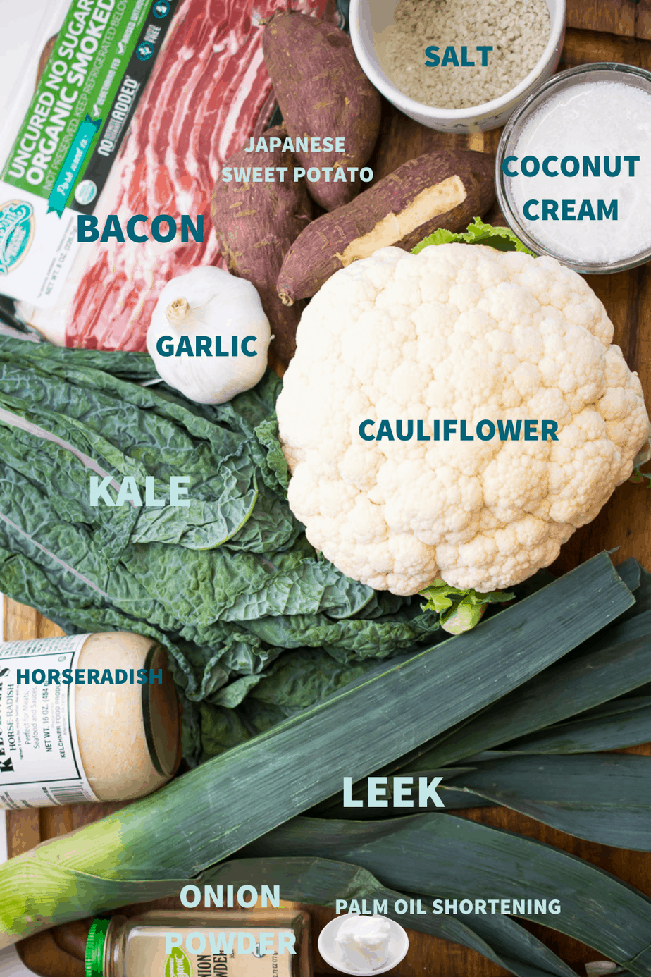 Cauliflower colcannon ingredients set out on table- salt, japanese sweet potato, coconut cream, bacon, garlic, cauliflower, kale, horseradish, leek, onion powder, palm oil shortening