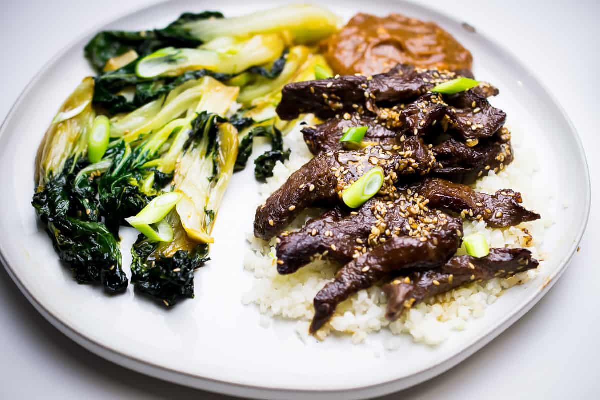 whole30 korean beef plate with bok choy and korean beef over cauliflower rice garnished with green onion, brown sauce on side