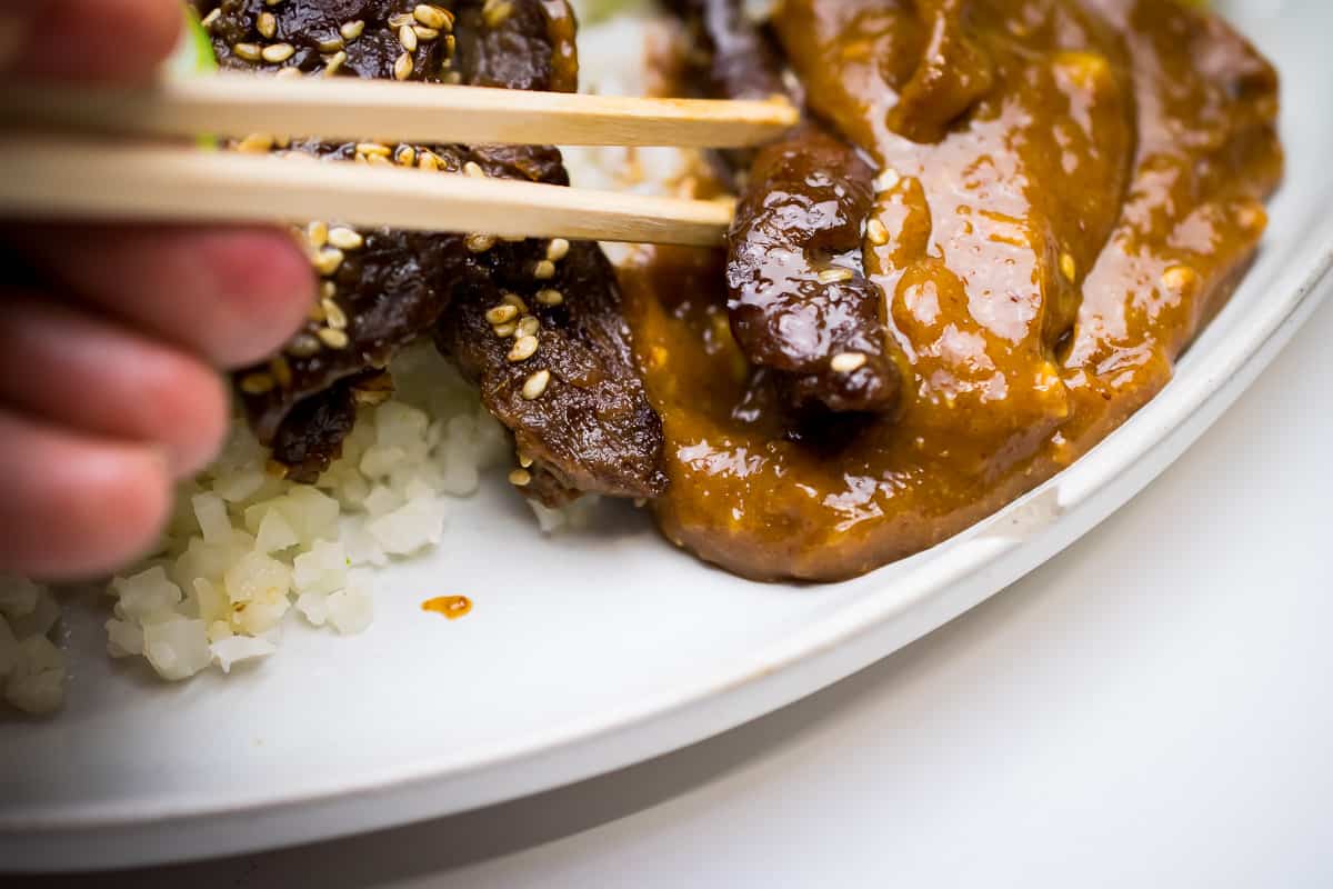 paleo korean beef close up of chop sticks dipping sliced beef into sauce