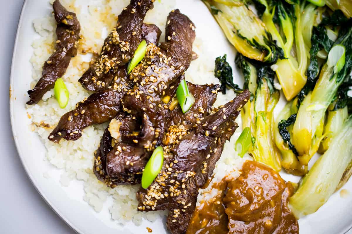 plate with bok choy and korean beef over cauliflower rice garnished with green onion, brown sauce on side