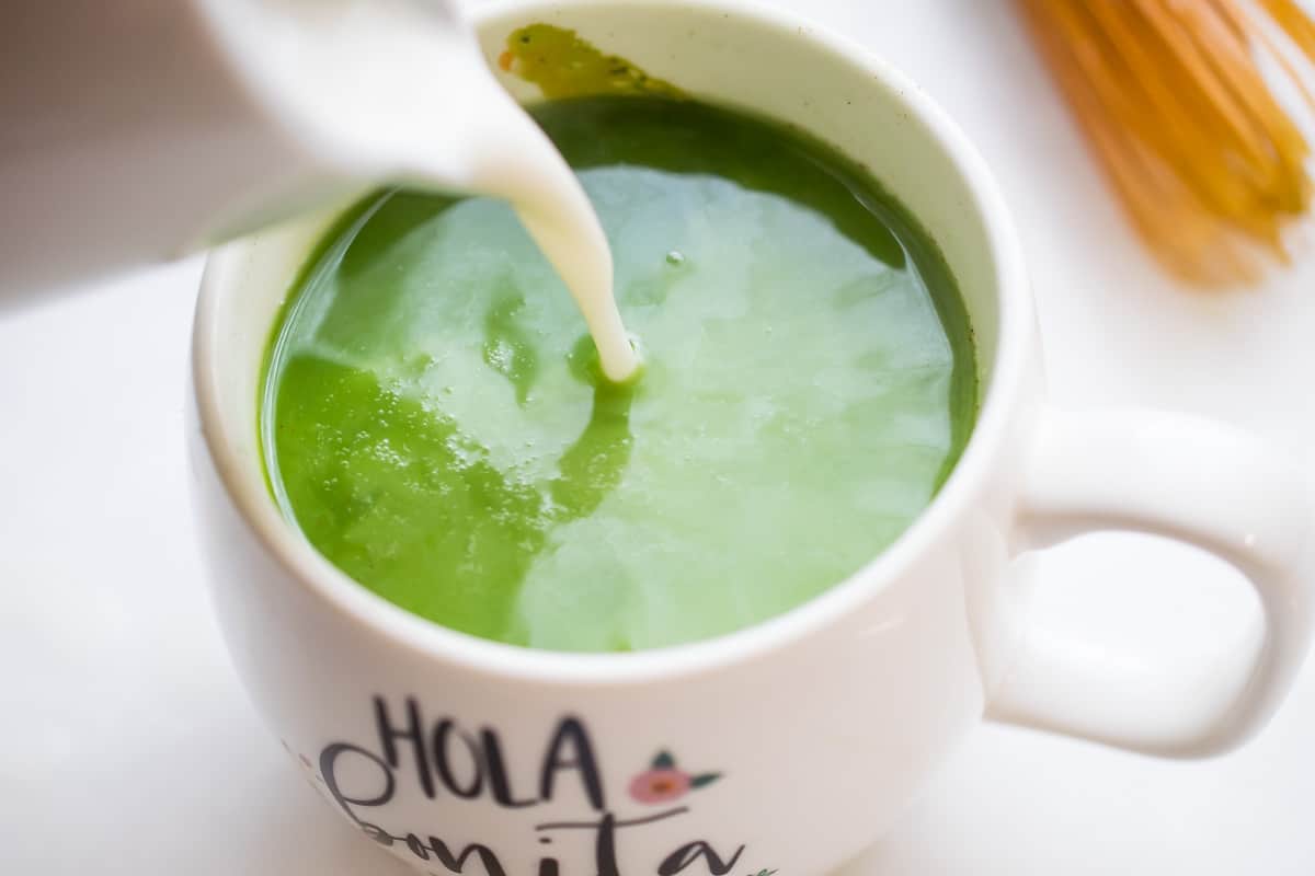 tigernut milk being poured into a bright green matcha beverage in a white mug