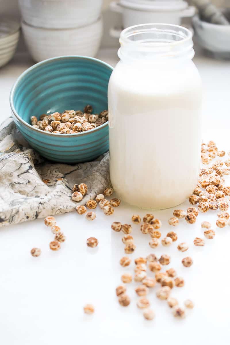 tiger nut milk in a jar, blue bowl with tiger nuts next to it and tiger nuts spread out on table