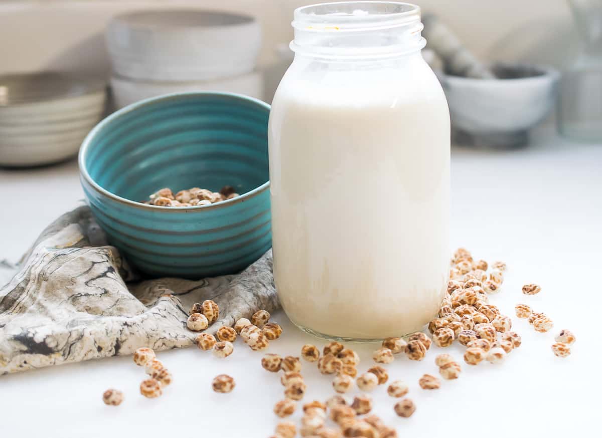 tiger nut milk in a jar, blue bowl with tiger nuts next to it and tiger nuts spread out on table