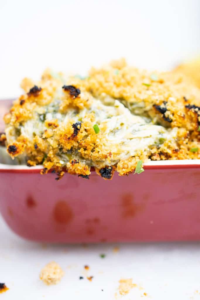 Cheesy dairy-free AIP Chicken Casserole with spinach, baked and bubbly in a red casserole dish, topped with crunchy pork panko.