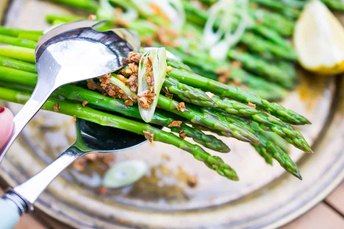 AIP ASPARAGUS SALAD being grabbed in tongs. in the background more asparagus salad on dish with lemon