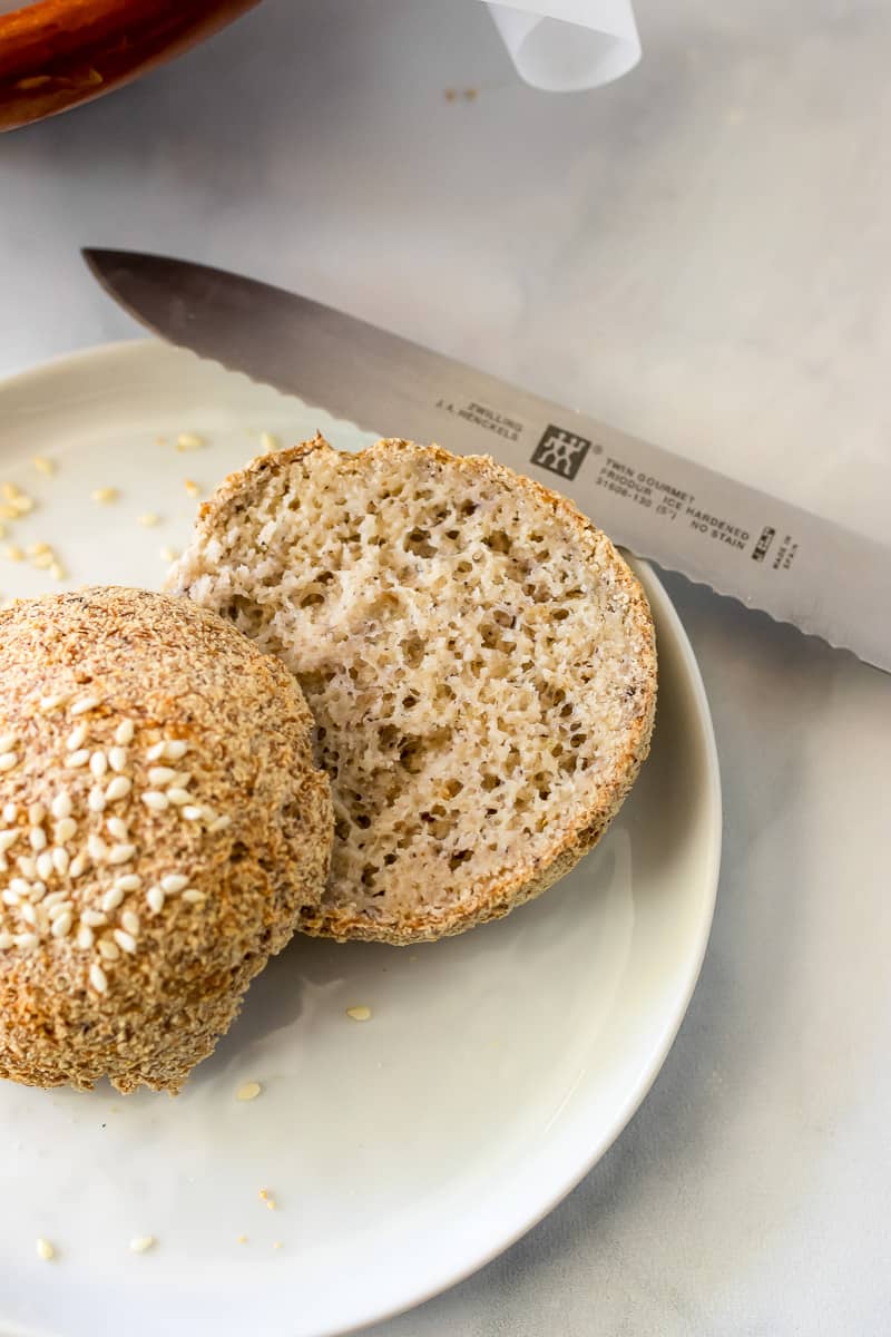 A Nut Free Keto Roll sliced in half on a white plate with a serrated knife.