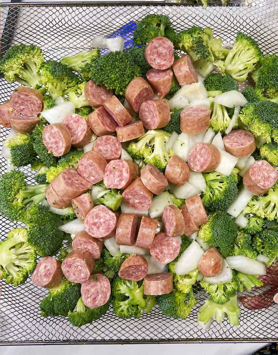 broccoli, onion, and brats chopped up on the air fryer tray ready to get toasty