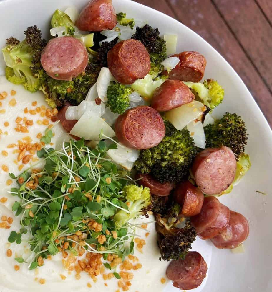 air fryer broccoli and brats with chopped onion on a white dish garnished with microgreens