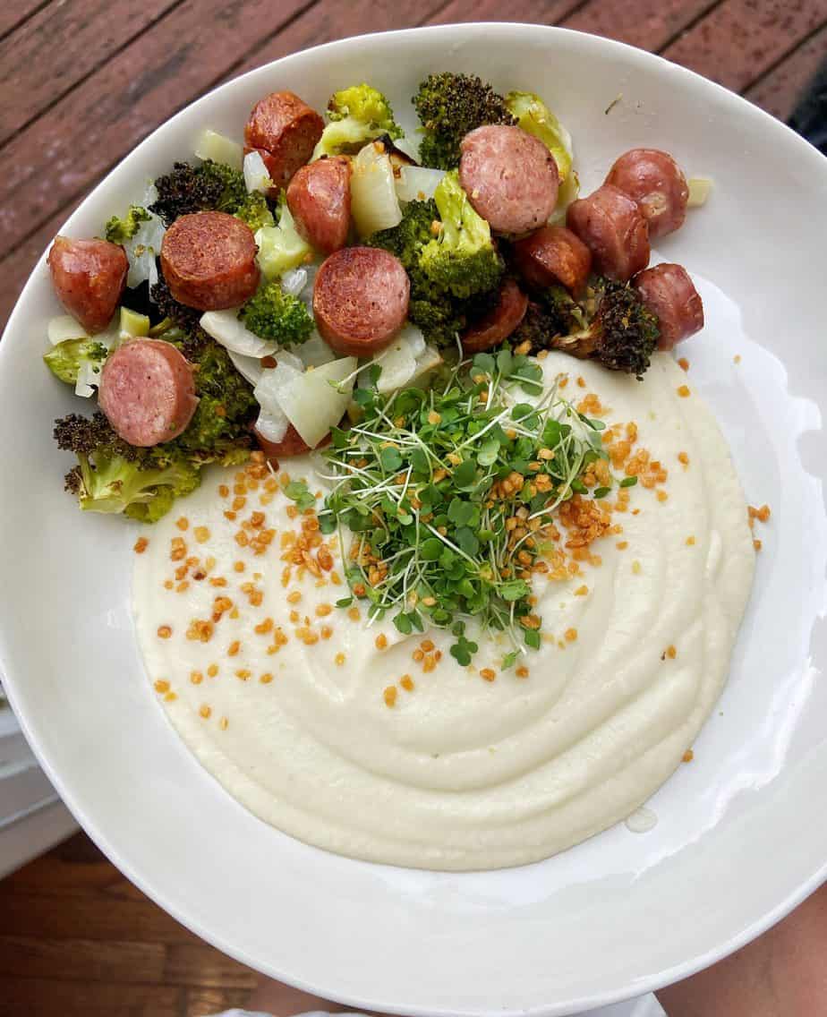 chopped up brats with broccoli and onion next to whipped cauliflower puree garnished with microgreens