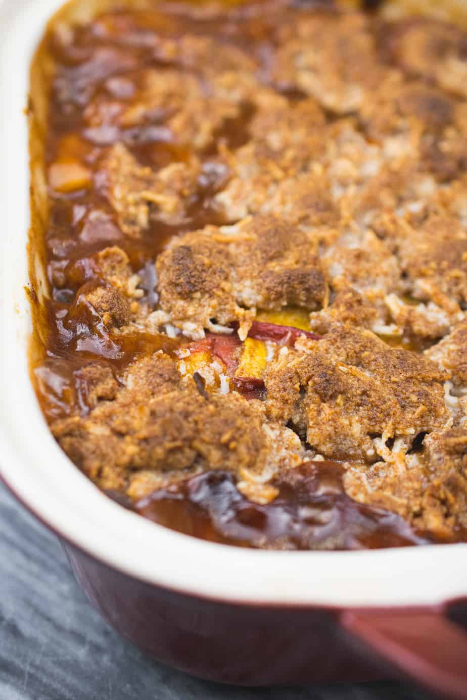 close up of baked aip peach cobbler. light and dark brown coconut covers the orange peaches underneath. 