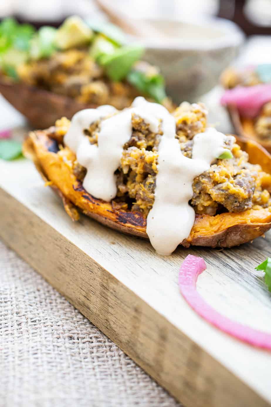 one stuffed sweet potato skin at the forefront with a generous dose of sauce drizzled on top. 