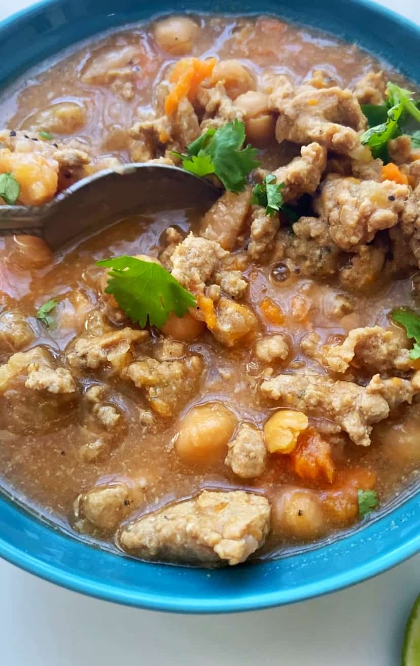 close up of turkey and garbanzo soup in blue bowl garnished with cilantro