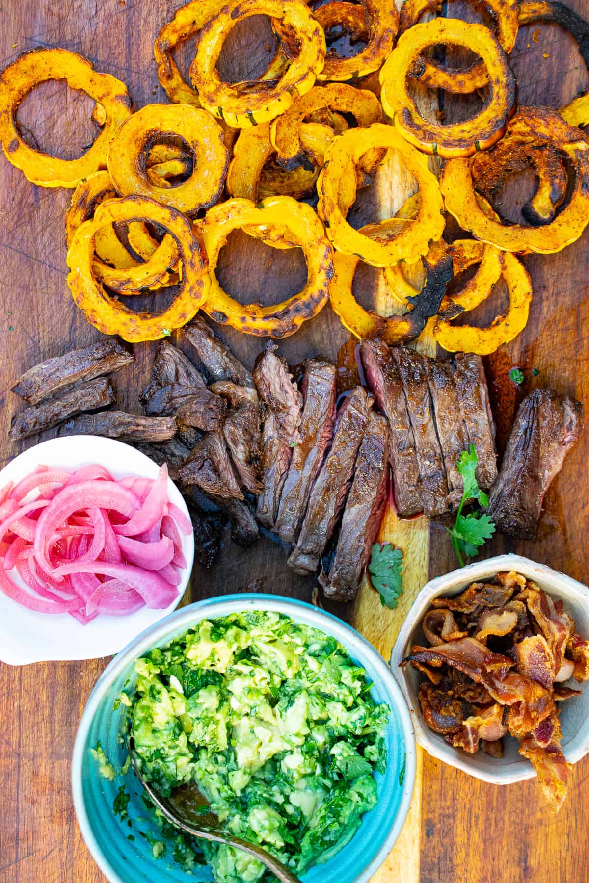 delicata squash chips on a cutting board with sliced steak, guacamole on a bowl and other toppings