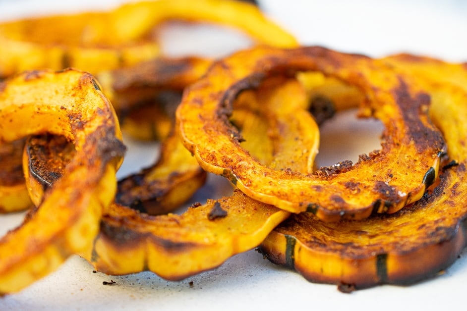 sliced and air fried delicata squash thats heavily seasoned piled on a plate