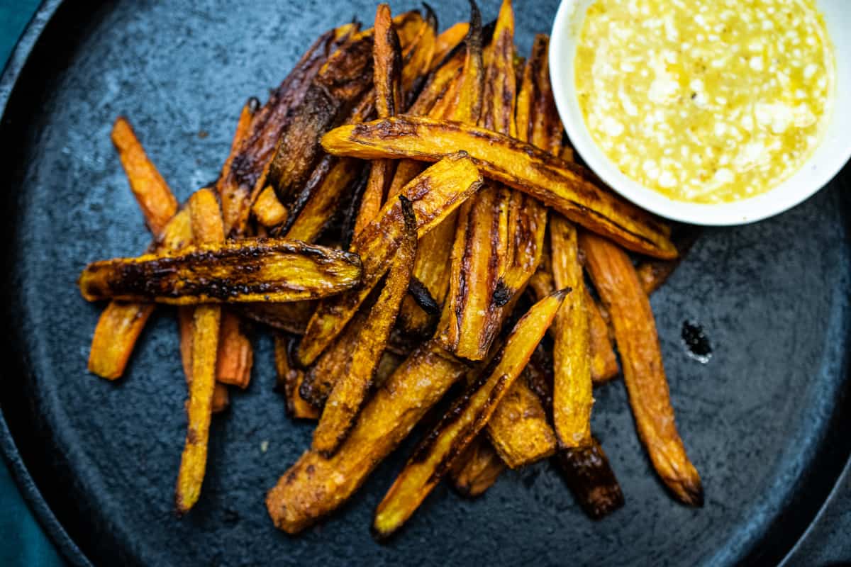 pile of crispy roasted carrots on cast iron with a yellow dipping sauce